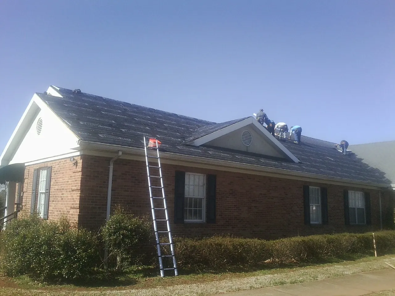 Crew tearing shingles off a brick ranch roof with a ladder set — Emergency Roof Repair work by our crew in Cloverdale